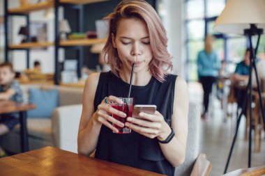 Smartphone kullanarak ve bir kafede bir kokteyl içme çekici kadın.