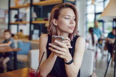 Smartphone kullanarak ve bir kafede bir kokteyl içme çekici kadın.