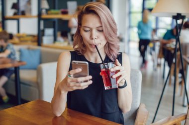 Smartphone kullanarak ve bir kafede bir kokteyl içme çekici kadın.