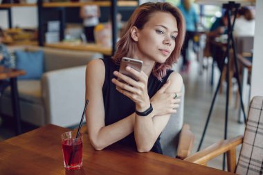 Smartphone kullanarak ve bir kafede bir kokteyl içme çekici kadın.