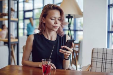 Smartphone kullanarak ve bir kafede bir kokteyl içme çekici kadın.