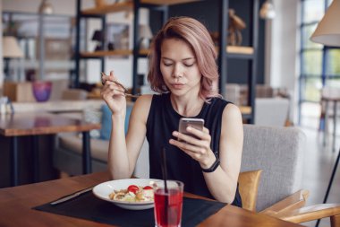 Smartphone kullanarak ve bir kafede yemek çekici kadın.
