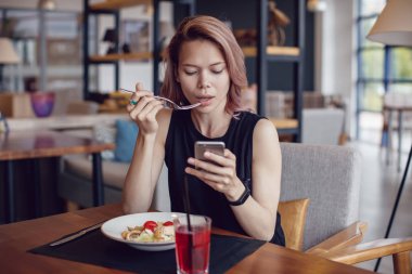 Smartphone kullanarak ve bir kafede yemek çekici kadın.