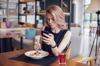 Smartphone kullanarak ve bir kafede yemek çekici kadın.