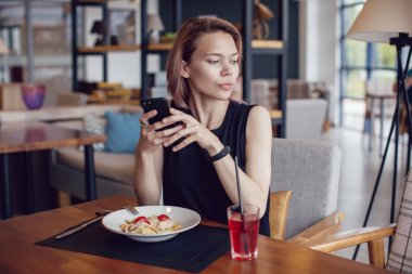 Smartphone kullanarak ve bir kafede yemek çekici kadın.