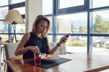 Smartphone kullanarak ve bir kafede yemek çekici kadın.