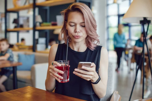 Smartphone kullanarak ve bir kafede bir kokteyl içme çekici kadın.