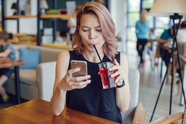 Smartphone kullanarak ve bir kafede bir kokteyl içme çekici kadın.