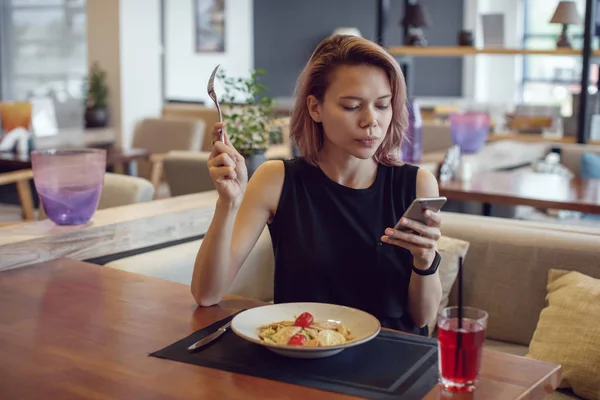 Donna attraente utilizzando smartphone e mangiare in un caffè . — Foto Stock