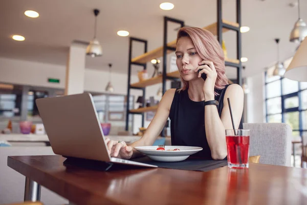 Mujer de negocios come en un café y utiliza un teléfono inteligente y un ordenador portátil . — Foto de Stock