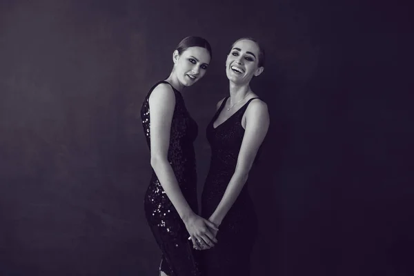 Дві красиві жінки в чорній сукні нічної моди позують на чорному тлі . — стокове фото