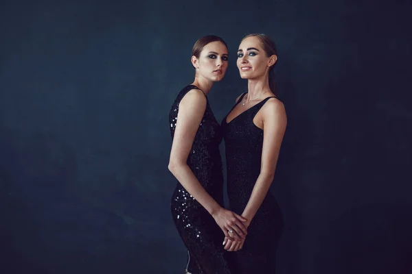 两个美丽的女人在黑色的夜时尚礼服摆在黑色的背景. — 图库照片