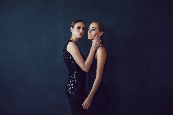 Two beautiful women in black night fashion dress posing on a black background. — Stock Photo, Image