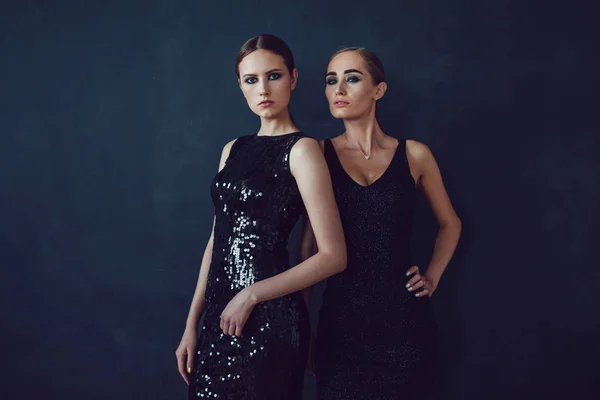 Two beautiful women in black night fashion dress posing on a black background. — Stock Photo, Image