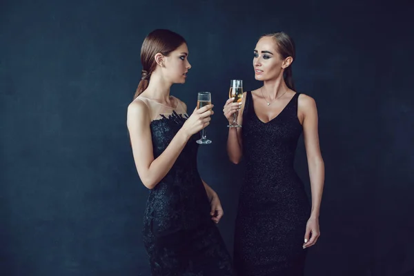 Mulheres atraentes em vestidos de cocktail estão segurando copos de champanhe, falando e sorrindo . — Fotografia de Stock