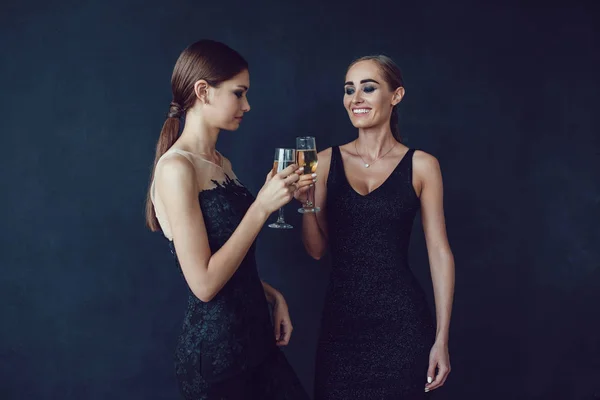 Mulheres atraentes em vestidos de cocktail estão segurando copos de champanhe, falando e sorrindo . — Fotografia de Stock