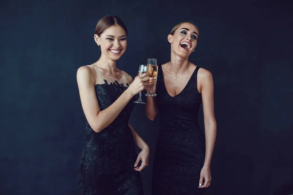 Mulheres atraentes em vestidos de cocktail estão segurando copos de champanhe, falando e sorrindo . — Fotografia de Stock