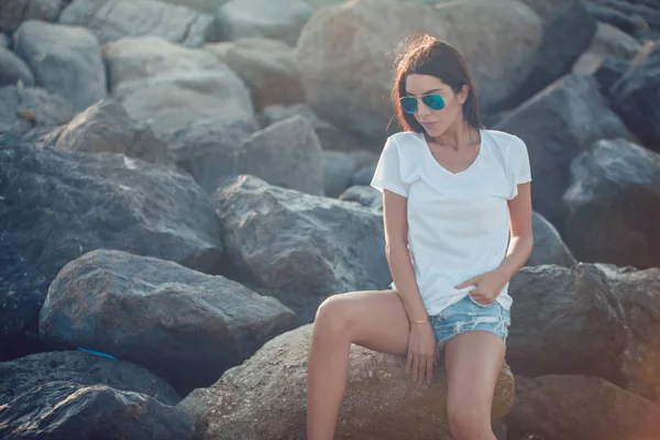 Menina em uma camiseta branca e óculos de sol no fundo de pedras. Mock-up . — Fotografia de Stock