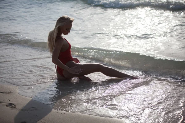 Sexy dziewczyna leży w czerwony strój kąpielowy w pobliżu oceanu. Widok z tyłu. — Zdjęcie stockowe