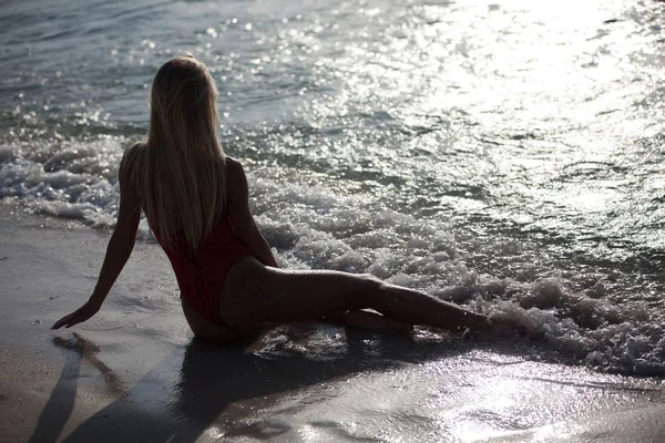性感的女孩躺在一个红色的泳衣附近的海洋。后视图. — 图库照片
