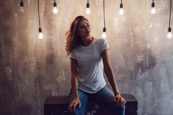 Sexy vrouw in een witte T-shirt op een grijze achtergrond met lampen. Mock-up. — Stockfoto