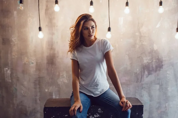 Sexy woman in a white T-shirt on a gray background with light bulbs. Mock-up. — Stock Photo, Image