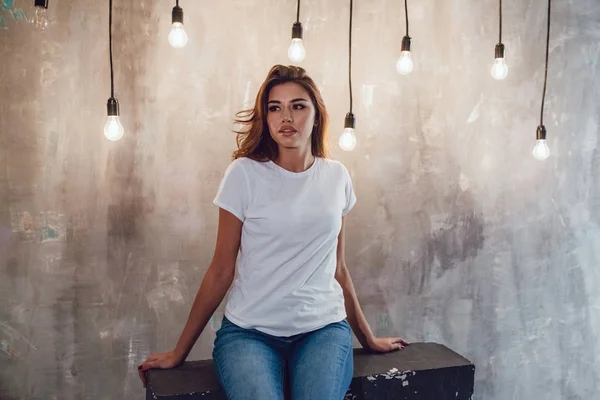 Mujer sexy en una camiseta blanca sobre un fondo gris con bombillas. Mock-up . — Foto de Stock
