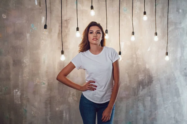 Mujer sexy en una camiseta blanca sobre un fondo gris con bombillas. Mock-up . —  Fotos de Stock