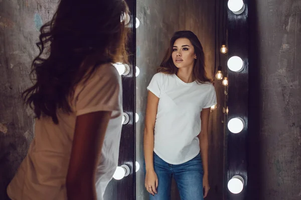 Sexy woman in a white t-shirt looks in the mirror. Mock-up. — Stock Photo, Image