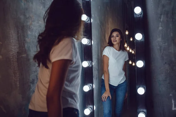 Sexy woman in a white t-shirt looks in the mirror. Mock-up. — Stock Photo, Image