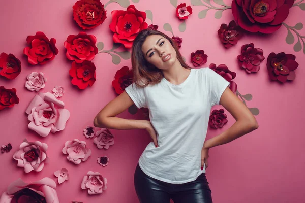 Mulher sexy em uma camiseta branca em um fundo rosa com flores . — Fotografia de Stock