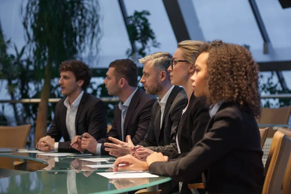 Een groep van mensen uit het bedrijfsleven zitten aan een tafel in een lijn en debatteren. — Stockfoto