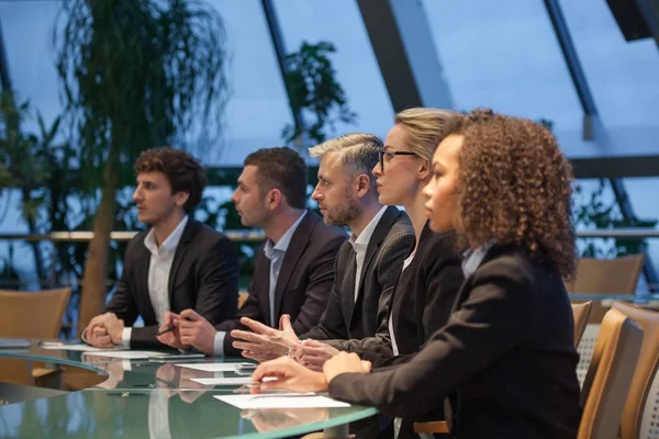 Een groep van mensen uit het bedrijfsleven zitten aan een tafel in een lijn en debatteren. — Stockfoto