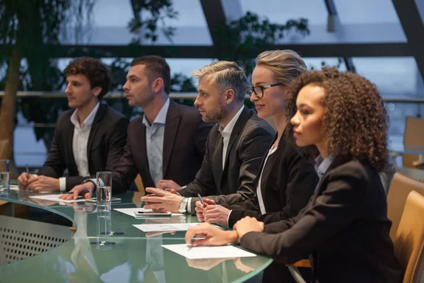 Een groep van mensen uit het bedrijfsleven zitten aan een tafel in een lijn en debatteren. — Stockfoto