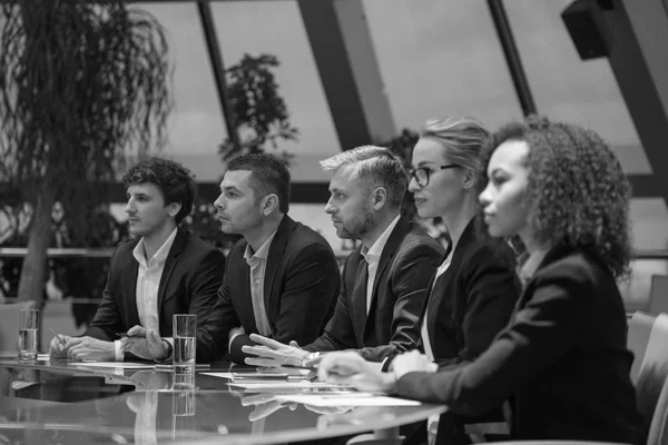 Een groep van mensen uit het bedrijfsleven zitten aan een tafel in een lijn en debatteren. — Stockfoto