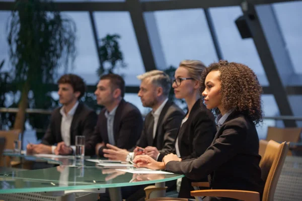 Een groep van mensen uit het bedrijfsleven zitten aan een tafel in een lijn en debatteren. — Stockfoto