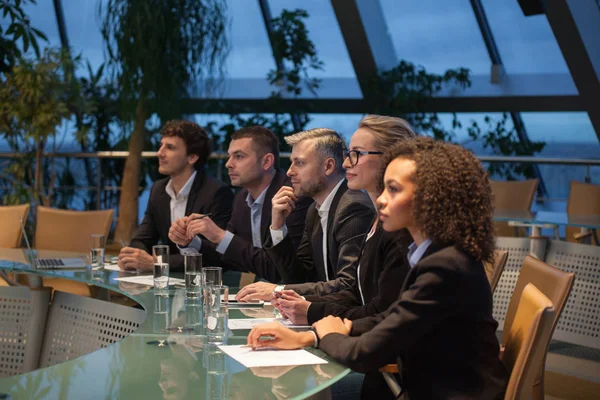 Een groep van mensen uit het bedrijfsleven zitten aan een tafel in een lijn en debatteren. — Stockfoto