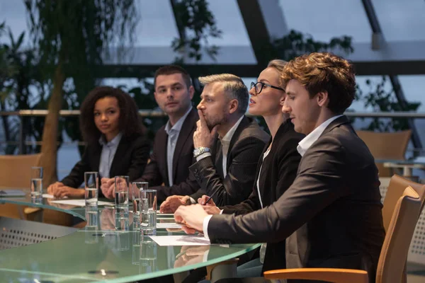 Een groep van mensen uit het bedrijfsleven zitten aan een tafel in een lijn en debatteren. — Stockfoto