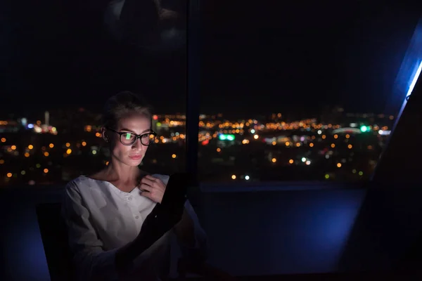 実業家は、夜の街の背景のオフィスの窓辺に座っているスマート フォンを使用してください。. — ストック写真