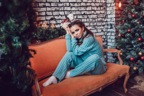 Vackra womanis sitter i soffan nära julgranen. Nytt år. — Stockfoto