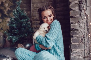 Çekici kız ellerinde şirin köpek yavrusu ile evde oturuyor. Noel.