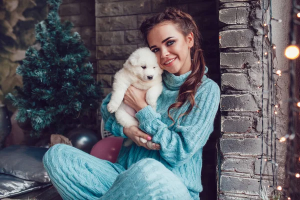 Attractive girl sits at home with cute puppy on hands. Christmas. — Stock Photo, Image