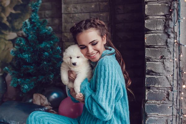 Attractive girl sits at home with cute puppy on hands. Christmas. — Stock Photo, Image