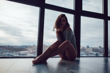 Gri elbise seksi kadın panoramik pencerenin yakınındaki katta oturur.