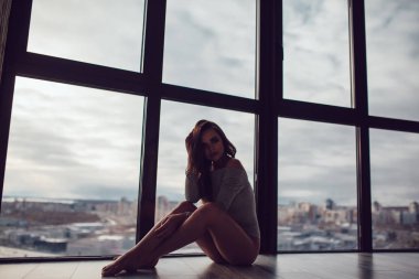 Gri elbise seksi kadın panoramik pencerenin yakınındaki katta oturur.