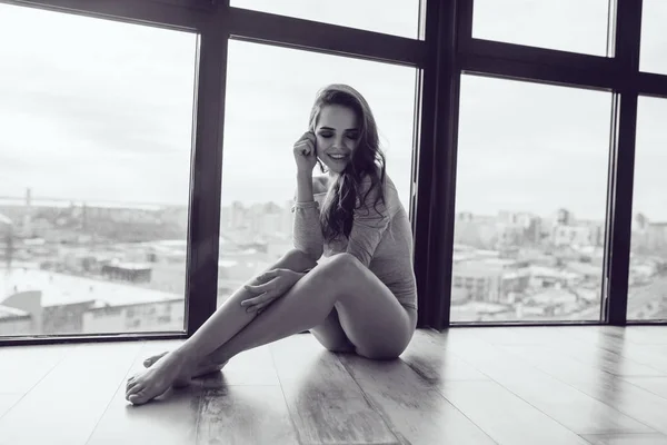 Sexy woman in gray bodysuit sits on the floor near the panoramic window. — Stock Photo, Image