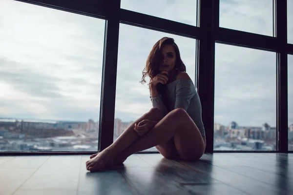 Gri elbise seksi kadın panoramik pencerenin yakınındaki katta oturur.