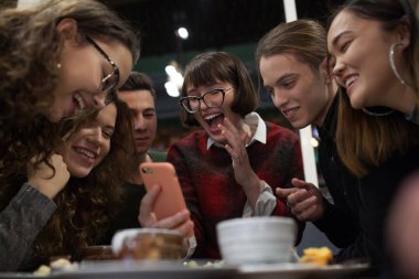 Pozitif gençler grup bir akıllı telefon kullanmak ve bir kafede vakit.