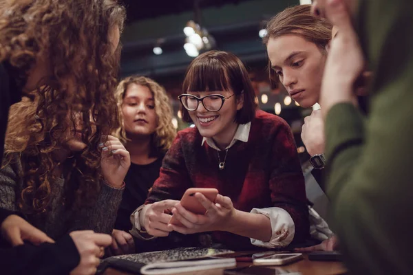 Gruppe av positive tenåringer bruker smarttelefon og tilbringer tid på kafe . – stockfoto