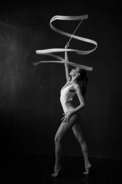 Güzel kadın jimnastikçi siyah bir zemin üzerine beyaz bir kurdele ile.